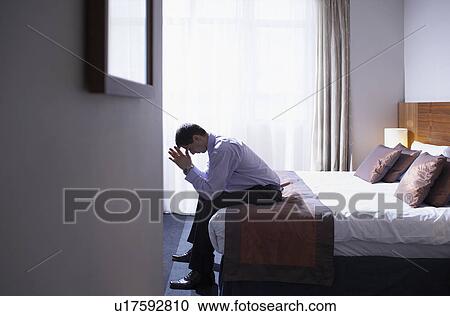 Stock Image - Man sitting on edge of bed with head in hands. Fotosearch