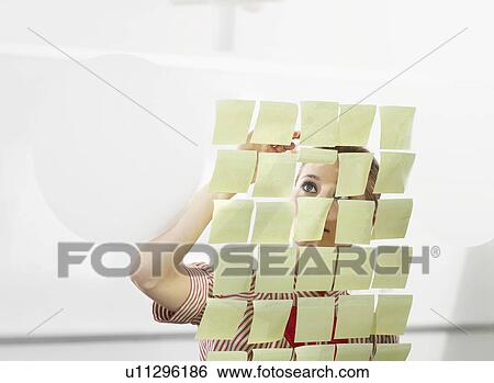 Stock Photograph - Post-It on glass and worker peering under. Fotosearch