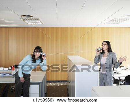 Two businesswomen using tin cans to communicate in office View Large Photo Image Stock Photo - Two businesswomen using tin cans to communicate in office. Fotosearch