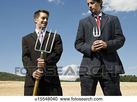 Stock Image - Two men holding garden tools next to each other.. Fotosearch