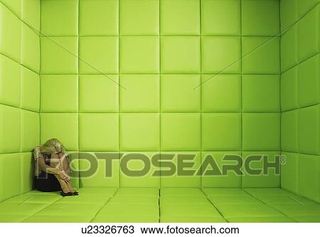 Stock Image - Woman crouching in corner of green padded cell. Fotosearch