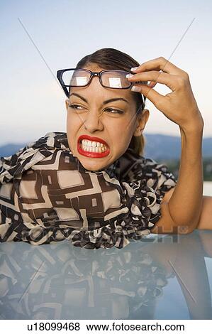 Stock Photo - Woman pushing eyeglasses up onto head scowling outdoors.. Fotosearch