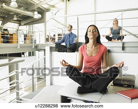 Young Adults Sitting On Office Desks In A Yoga Position Stock