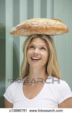 Stock Image - Young woman with loaf of bread on head.. Fotosearch