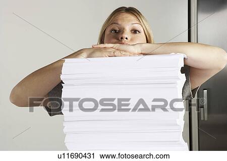 Stock Image - Young woman working from home with huge pile of paper.. Fotosearch
