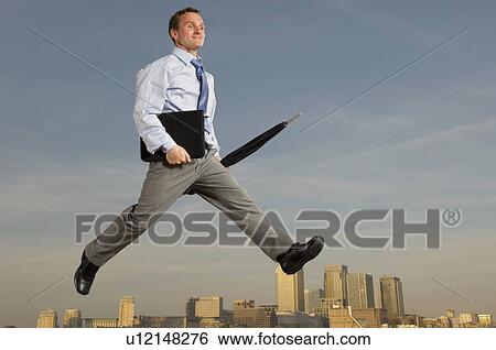 Stock Photograph - Business man striding across city skyline. Fotosearch