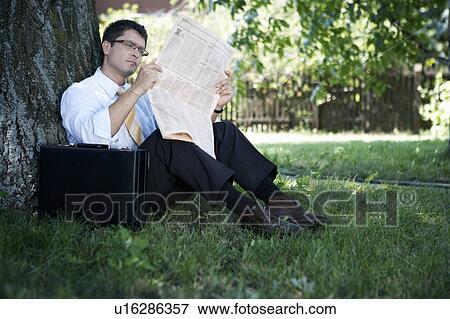 Stock Photo - Businessman laying by tree reading newspaper.. Fotosearch