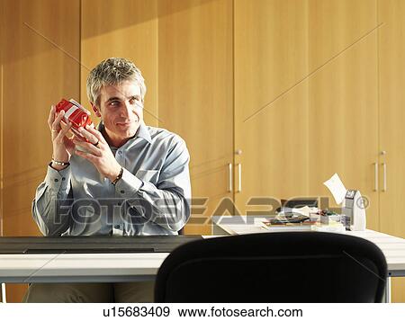 Stock Photo - Businessman sitting at desk shaking present, smiling. Fotosearch