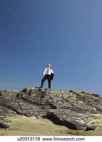 Stock Photo - Businessman standing on rock.. Fotosearch