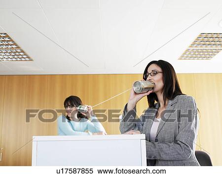 Stock Photography - Businesswoman using tin can to communicate with colleague, smiling. Fotosearch