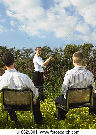 Stock Image - Group of businesspeople sitting on chairs in field.. Fotosearch