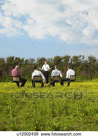 Stock Photo - Group of businesspeople sitting on chairs in field.. Fotosearch