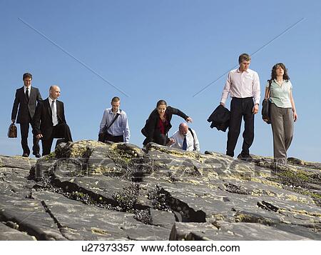 Stock Photo - Group of businesspeople walking across rock.. Fotosearch