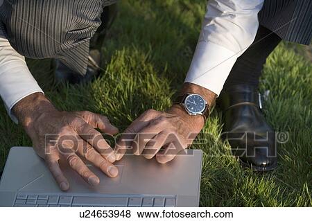 Man crouching on grass using laptop, close-up View Large Photo Image Stock Photo - Man crouching on grass using laptop, close-up. Fotosearch