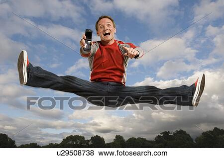 Stock Photo - Man jumping in the air holding his cell phone. Fotosearch