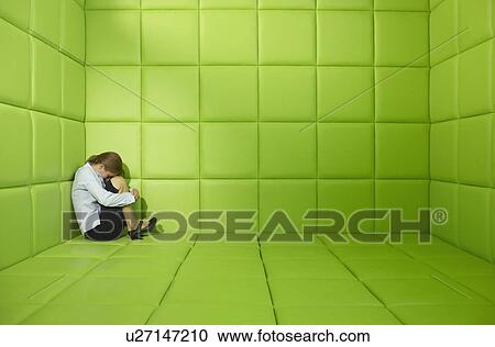 Stock Image - Woman crouched in a corner in a green padded cell. Fotosearch