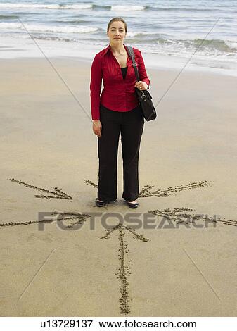 Stock Photo - Woman on beach with arrows in sand around her.. Fotosearch