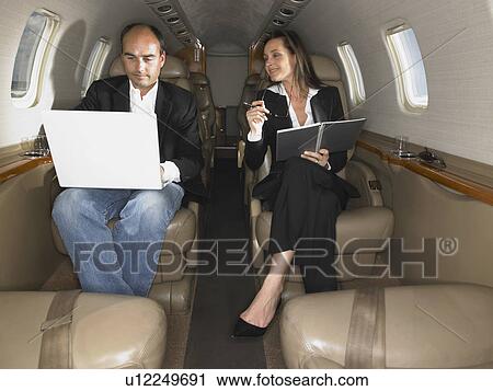 Stock Image - Businessman and businesswoman inside a private jet having a discussion.. Fotosearch