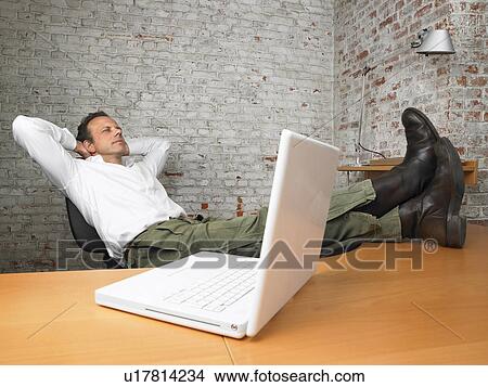 Picture - Businessman resting with feet on desk., Brussels, Belgium.. Fotosearch