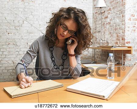 Stock Image - Businesswoman talking on the phone and writing., Brussels, Belgium.. Fotosearch