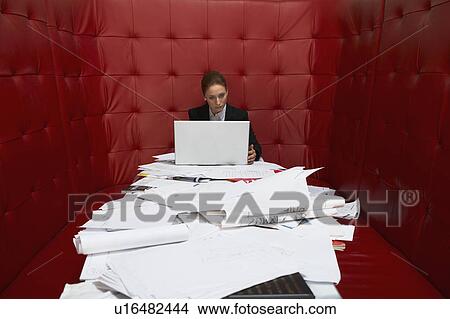Picture - Businesswoman working at a table with red seating. Fotosearch
