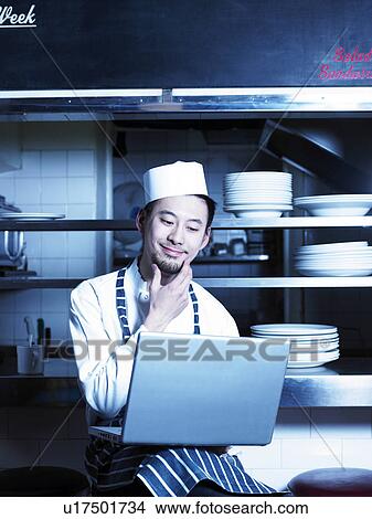 Chef looking at laptop in restaurant kitchen View Large Photo Image Picture - Chef looking at laptop in restaurant kitchen. Fotosearch