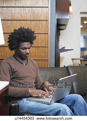 Man sitting on sofa using laptop View Large Photo Image Stock Image - Man sitting on sofa using laptop. Fotosearch