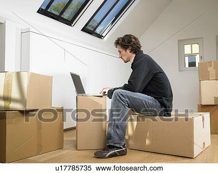 Stock Photography - Man sitting with laptop on moving box.. Fotosearch