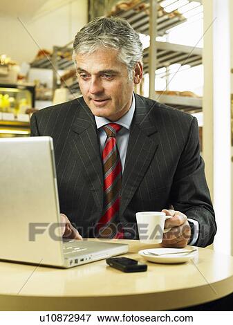 Stock Photo - Mature businessman sitting in cafe using laptop. Fotosearch