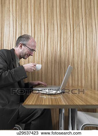 Stock Image - Mature man using laptop at restaurant table, side view. Fotosearch