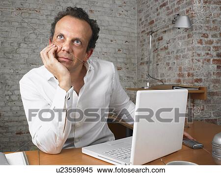 Stock Photography - Pensive businessman sitting at desk., Brussels, Belgium.. Fotosearch