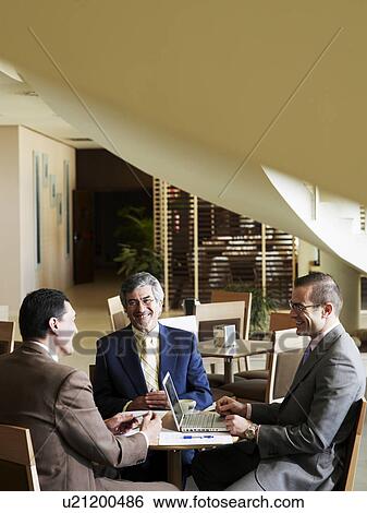 Stock Photograph - Three businessmen having meeting in restaurant, smiling. Fotosearch
