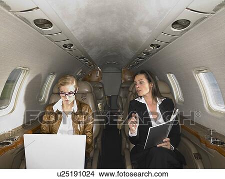 Picture - Two women in private jet having a discussion.. Fotosearch
