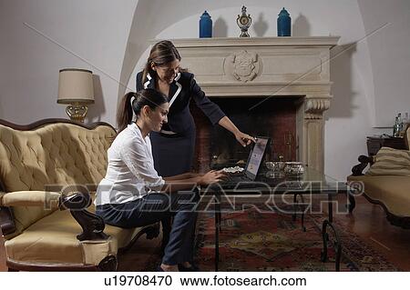Stock Image - Two women using laptop in living room. Fotosearch