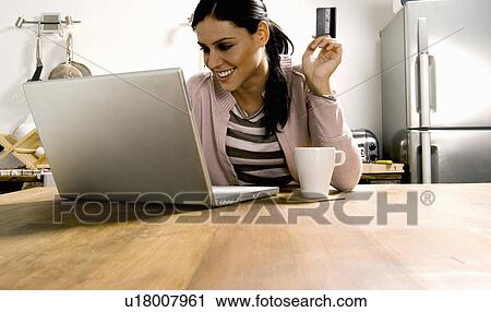 Stock Image - Woman looking at laptop with credit card.. Fotosearch