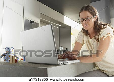 Stock Photography - Young business woman working from home kitchen.. Fotosearch