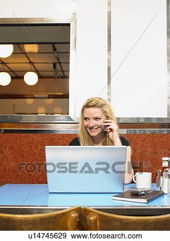 Young woman sitting with her laptop in a diner View Large Photo Image Stock Photo - Young woman sitting with her laptop in a diner. Fotosearch