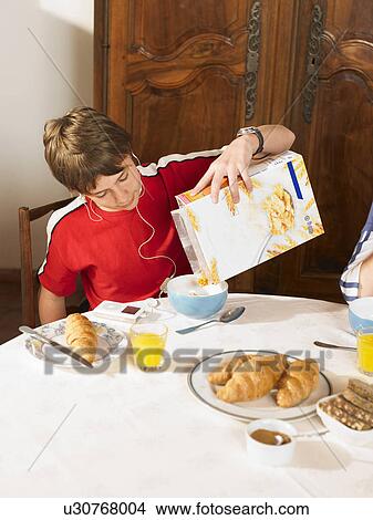 Picture - Boy (11-13) pouring cereal at breakfast table. Fotosearch