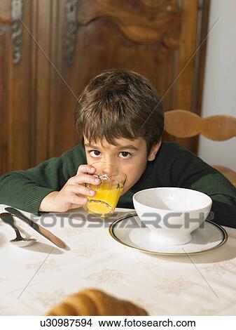 Picture - Boy (6-8) drinking orange juice at breakfast, portrait. Fotosearch