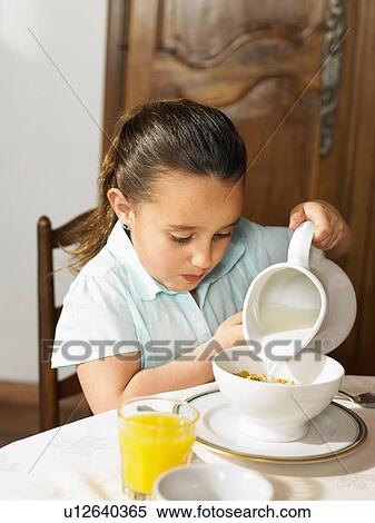 Stock Photography - Girl (4-6) pouring milk on cereal at breakfast. Fotosearch