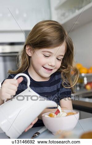 Stock Image - Girl putting milk into her bowl. Fotosearch