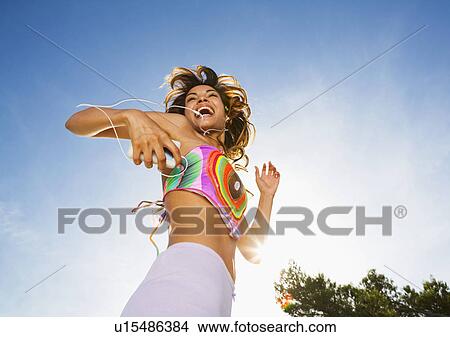 Picture - Energetic woman dances to MP3 player outdoors smiling.. Fotosearch