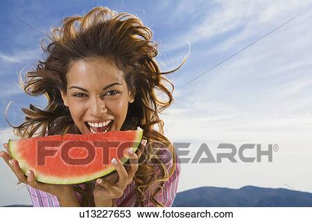 Stock Image - Woman laughing and eating watermelon outdoors.. Fotosearch