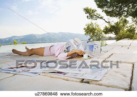 Stock Photo - Woman lying by infinity pool with newspaper over her face.. Fotosearch