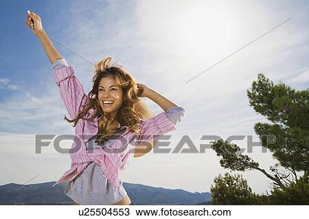 Stock Image - Woman outdoors smiling with arm in the air.. Fotosearch