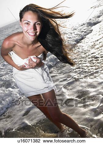 Stock Image - Woman standing in a towel at the beach smiling.. Fotosearch