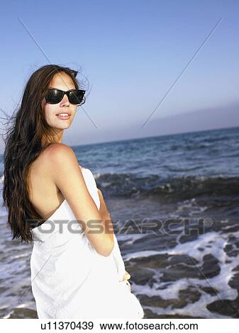 Stock Photo - Woman standing in a towel at the beach.. Fotosearch