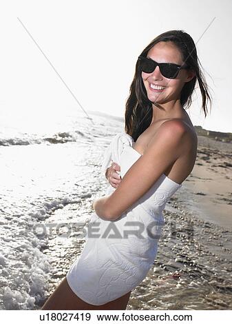 Stock Photo - Woman standing in a towel at the beach smiling.. Fotosearch