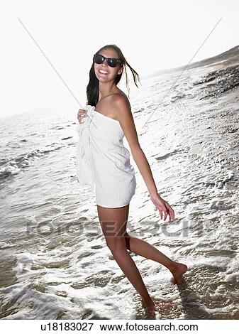 Stock Photo - Woman standing in a towel at the beach smiling.. Fotosearch