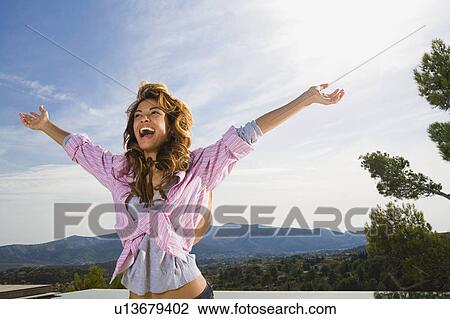 Stock Image - Woman with arms outstretched smiling by infinity pool.. Fotosearch